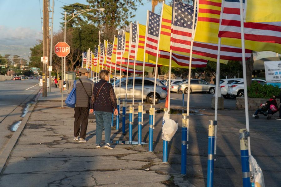 An old couple stands infront of the venue with the Vietnam and American flags
