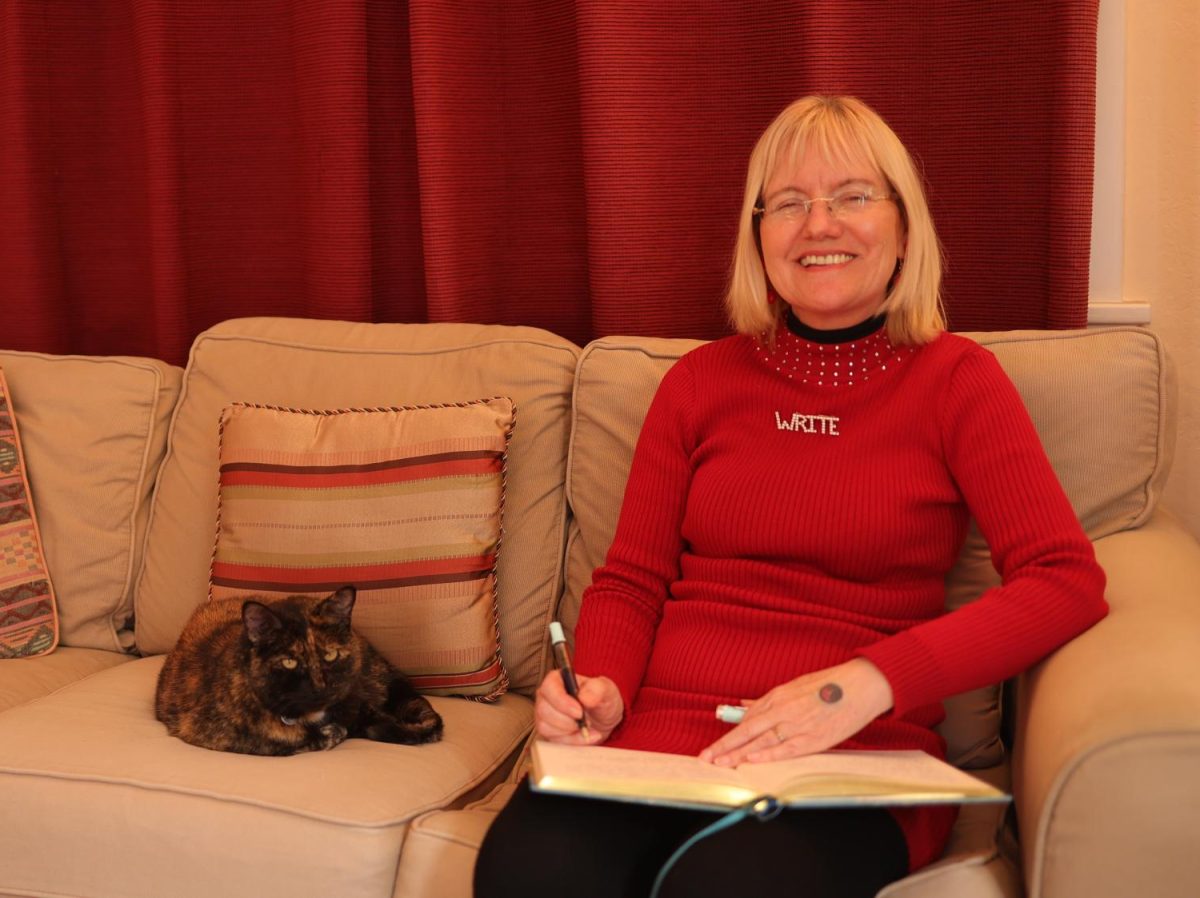 Lita Kurth, author and English professor at De Anza, smiles next to her cat, Mimi, while she writes in her journal in her home on Feb. 26.