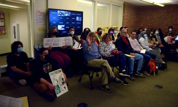 Members of the public sit in the designated public area, several with signs.