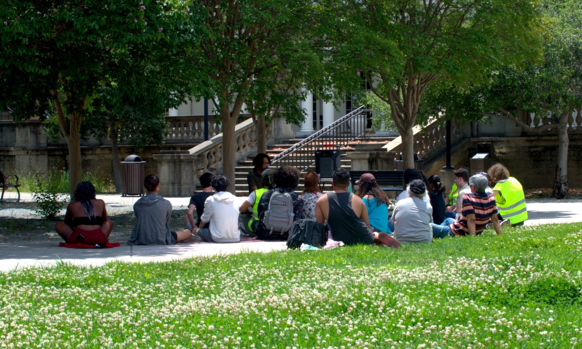 A+group+of+about+20+students+listen+and+ask+as+the+speaker%2C+only+identified+as+Sami%2C+talks+about+the+connections+between+Black+liberation+and+Palestinian+liberation+at+the+Sunken+Garden+on+June+18.
