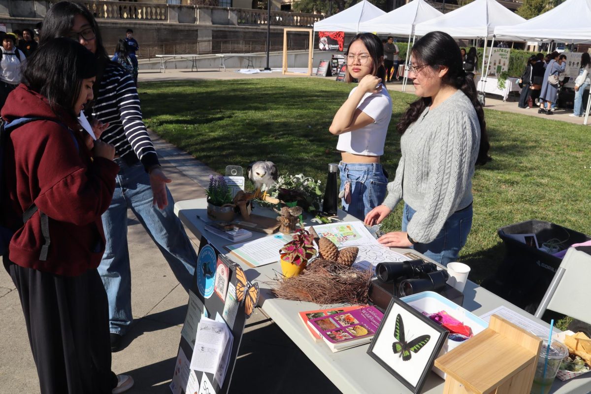 Zero Waste & Climate Awareness Club officers stand around the club's table and point at its information board and signup sheet in the Sunken Garden at Winter Club Day on Jan. 22.